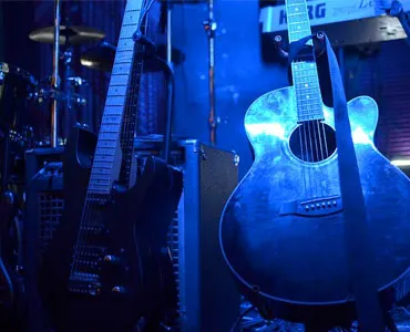 Acoustic guitar on a stage lit in blue, with a drum kit behind