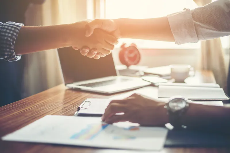 Two people shaking hands across a desk of documents