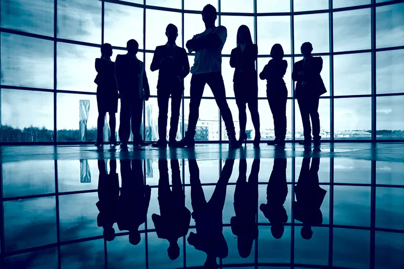 Silhouettes of a group of people standing together in front of tall windows