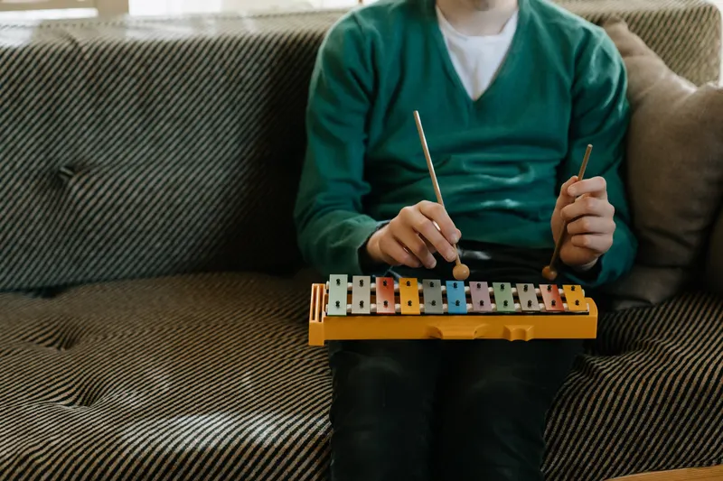 A child sitting on a sofa playing a toy xylophone
