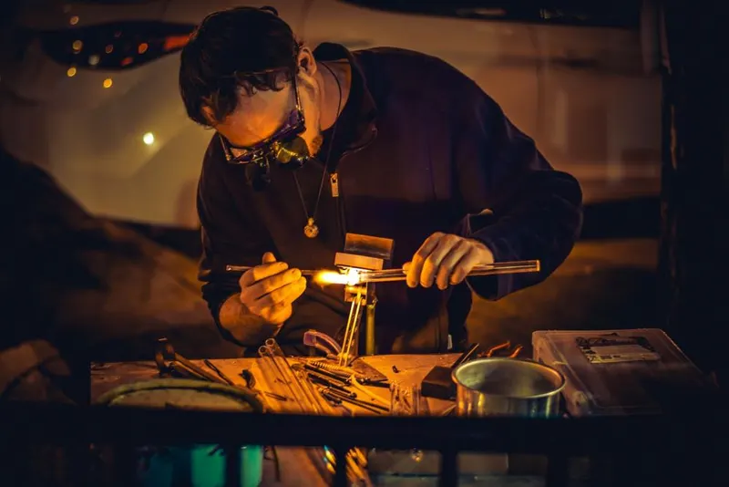 A glassmaker working with a torch at a workbench
