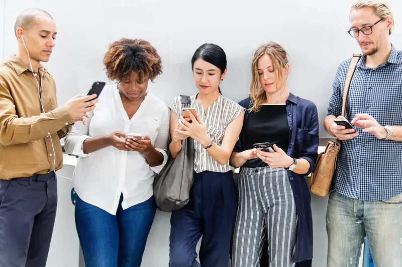 Five people standing side by side, each looking at a mobile phone
